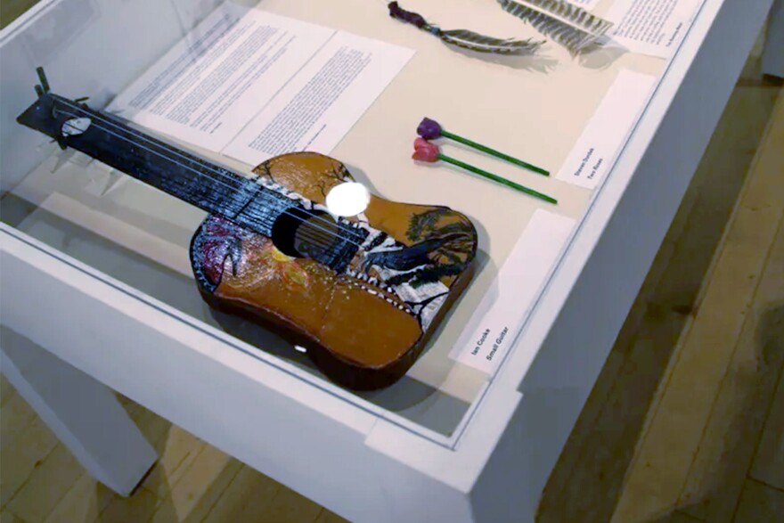 The guitar on the left is made of cardboard that Ian Cooke scrounged from legal pads. He sent it to his mother, Linda Cusano, who added the painted images on the outside.