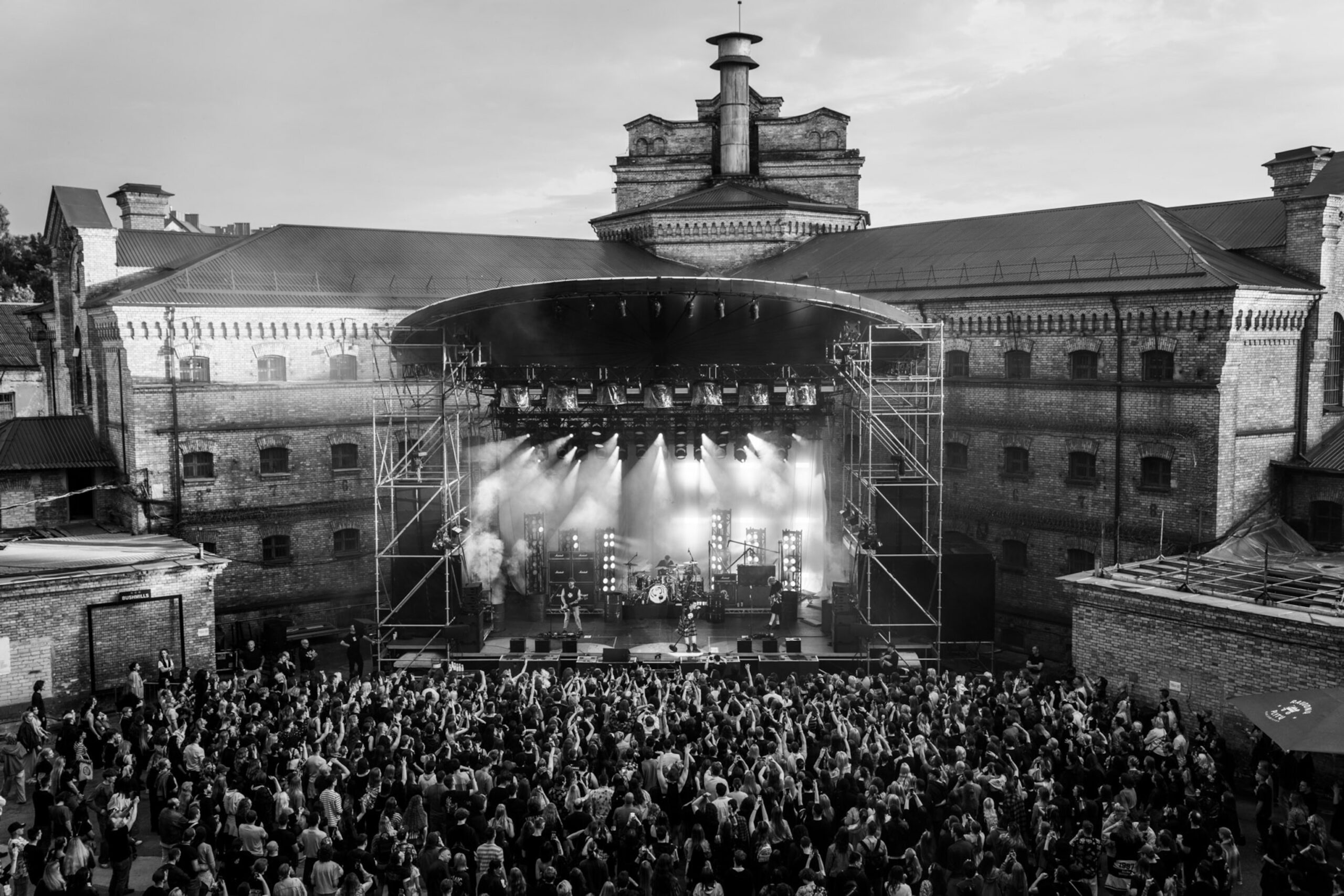 A massive concert crowd in front of a stage at the Lukiškės Prison 2.0. courtyard.