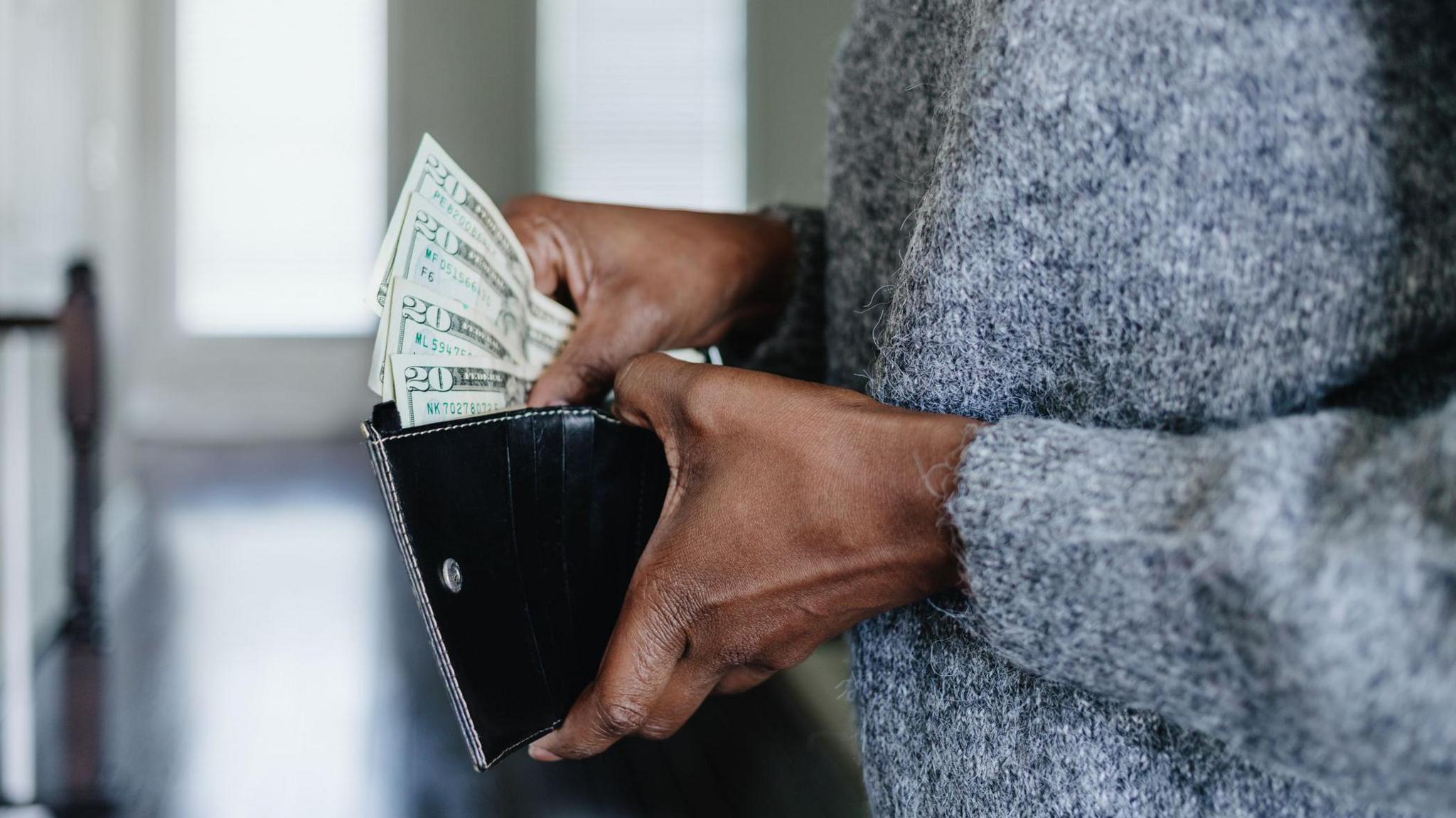 A cropped image showing the hands of a woman holding a wallet and fanning out $20 bills 