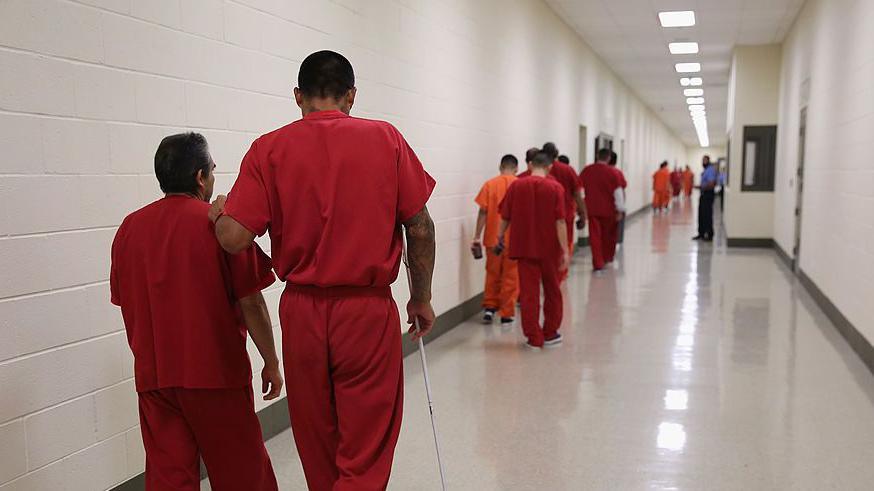 Migrant detainees in red jumpsuits walk down a hall at an ICE detention centre in Adelanto, California in 2013 that was run by GEO Group 