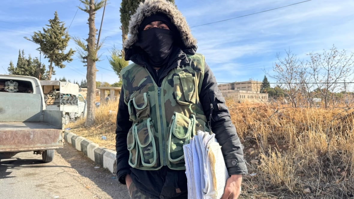 A man holds a stack of documents while wearing a balaclava and hood.