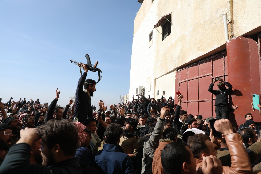 DAMASCUS, SYRIA - DECEMBER 9: A man holds a rifle as people gather at Sednaya Prison, where thousands of people were said to be detained and tortured by the Assad regime over the last decade, as families came to find information about detained and missing relatives on December 9, 2024 in Damascus, Syria. Sednaya prison (also spelled Saydnaya) was among the prisons liberated over the weekend as rebel forces in Syria seized the capital from longtime ruler Bashar al-Assad, who was reported to have fled the country. Syria has been mired in a multi-party civil war since 2011, sparked by the Arab Spring uprisings. (Photo by Ali Haj Suleiman/Getty Images)