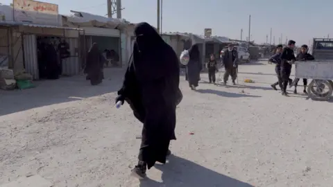 BBC A woman walking in the al-Hol camp in north-eastern Syria