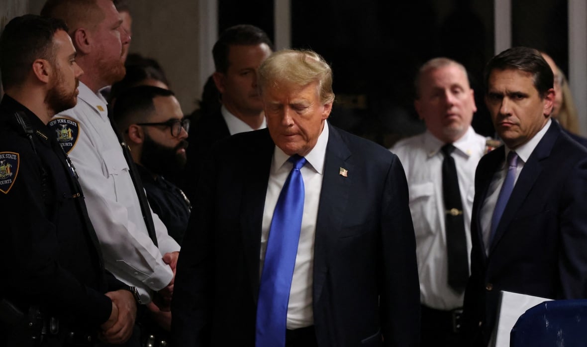 A man in a navy suit with a light blue tie appears defeated as he walks out of a courthouse.