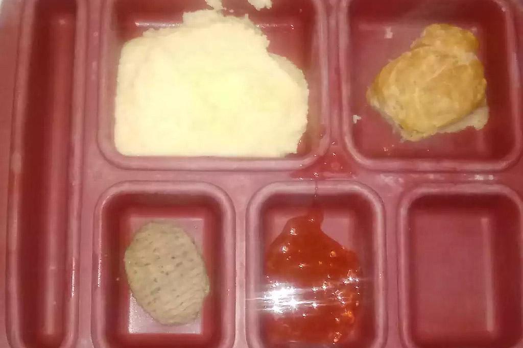 A red food tray shows several compartments with what looks like mashed potatoes, a biscuit, and jam. 