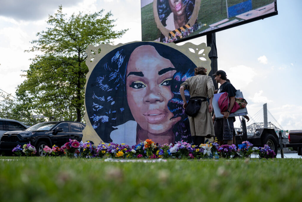 Protesters and volunteers prepare a Breonna Taylor art installation by laying posters and flowers before the 