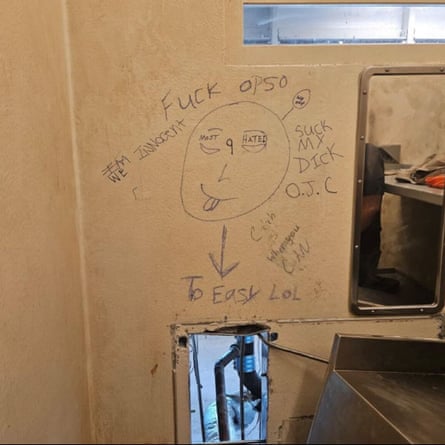 an opening in wall of jail cell with drawings and messages such as 'we innocent' and 'catch us when you can' written on the wall