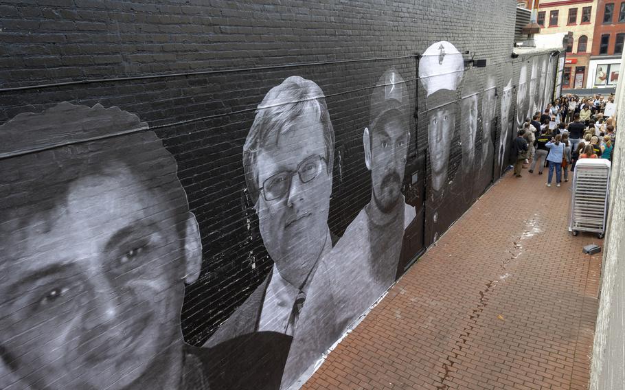 Mural of people’s faces on the side of a building with a group of people gathered in the background.