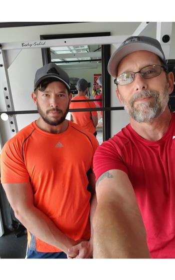 Two men in baseball caps and T-shirts pose for a photo with a mirror behind them.