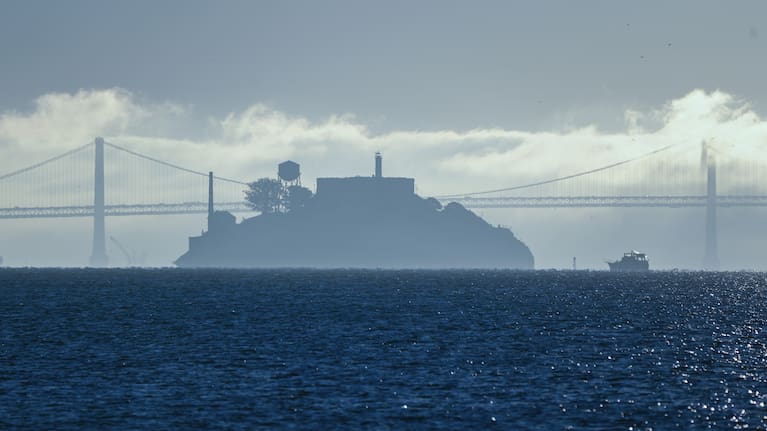 A boat makes its way toward Alcatraz Island with the San Francisco-Oakland Bay Bridge in the background.
