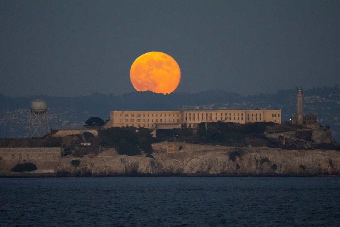 A full moon is seen behind a prison located on an island.