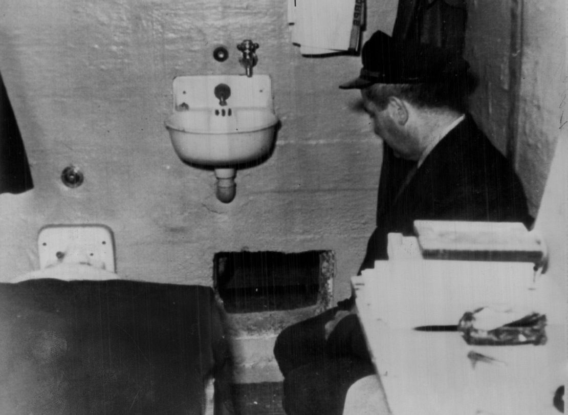 A prison guard kneels by a hole in Frank Morris' prison cell through which he, John and Clarence Anglin escaped. Prison officials reported that the hole was dug with broken spoons.