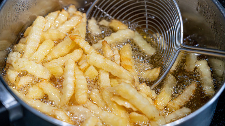 Crinkle fries in boiling oil being scooped